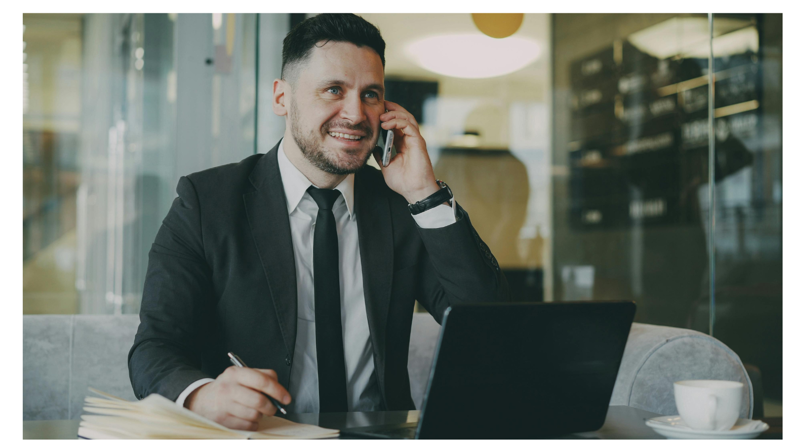 Business man on the phone with laptop, notepad and pen in hand.