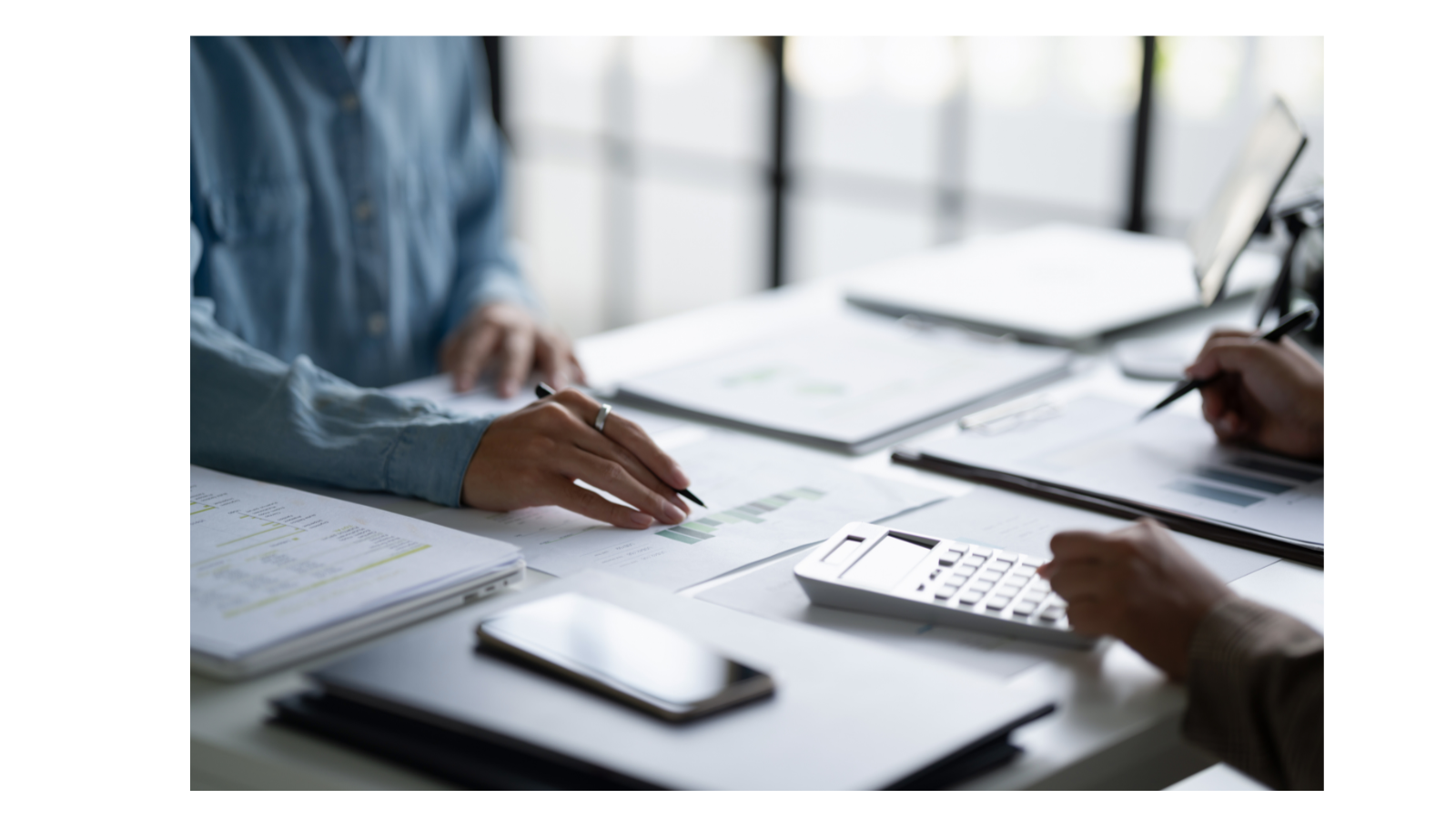 Two people are at a desk having a discussion, with documents, pen and calculator on the desk.
