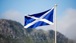 A Scottish flag on a pole in front of a view of a mountain.