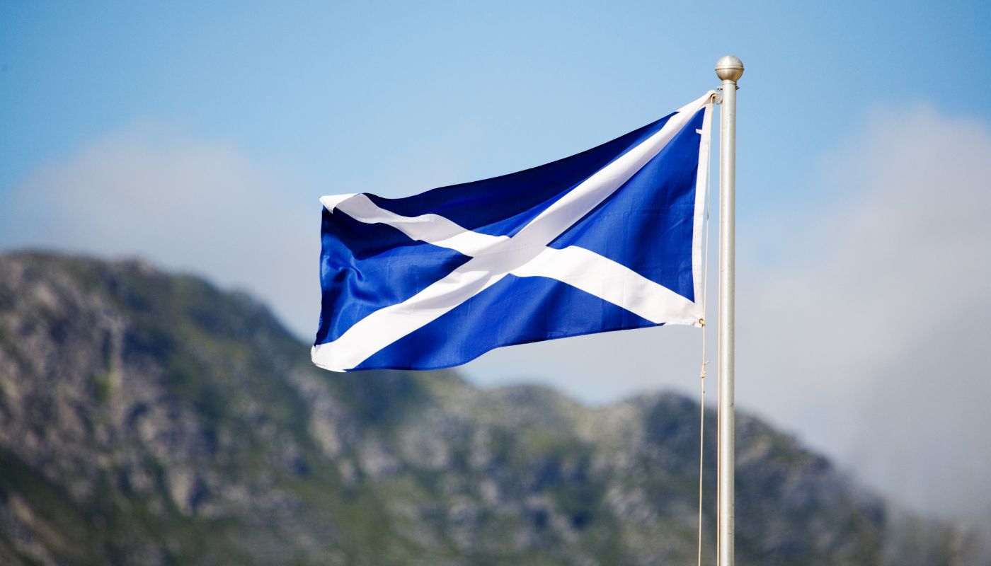 A Scottish flag on a pole in front of a view of a mountain.
