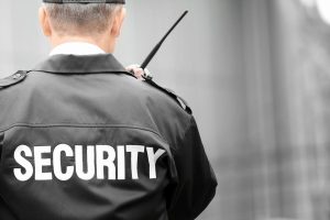 A security guard talking on his walkie talkie and wearing a cap.