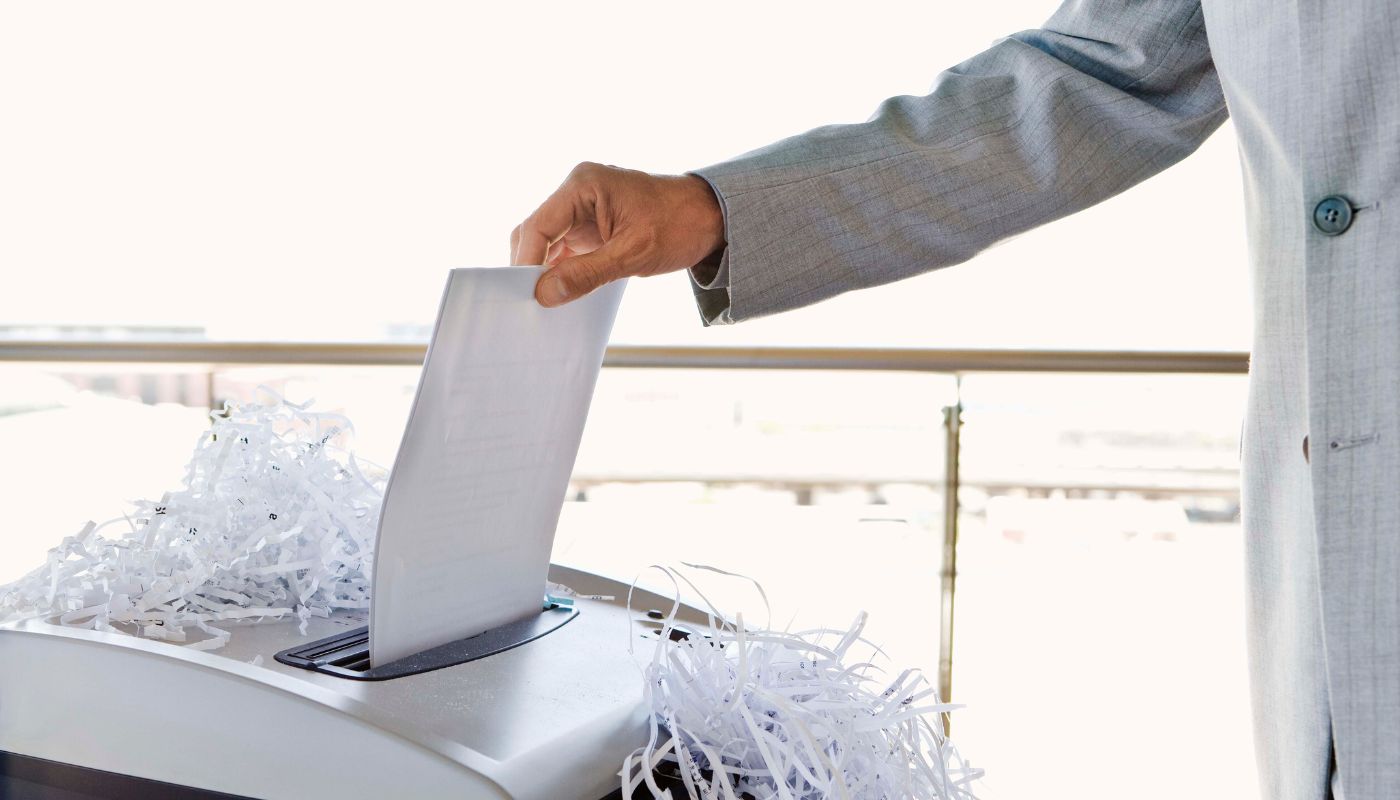 A man in a suit is shredding paper in a machine to get rid of any data.