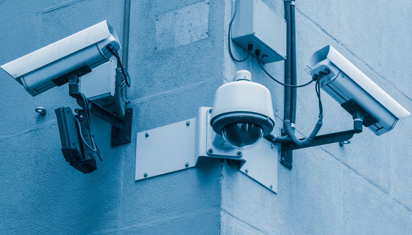 There are three cameras on a wall outside looking in all different directions.