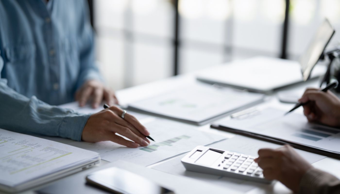 Two people are at a desk having a discussion, with documents, pen and calculator on the desk.