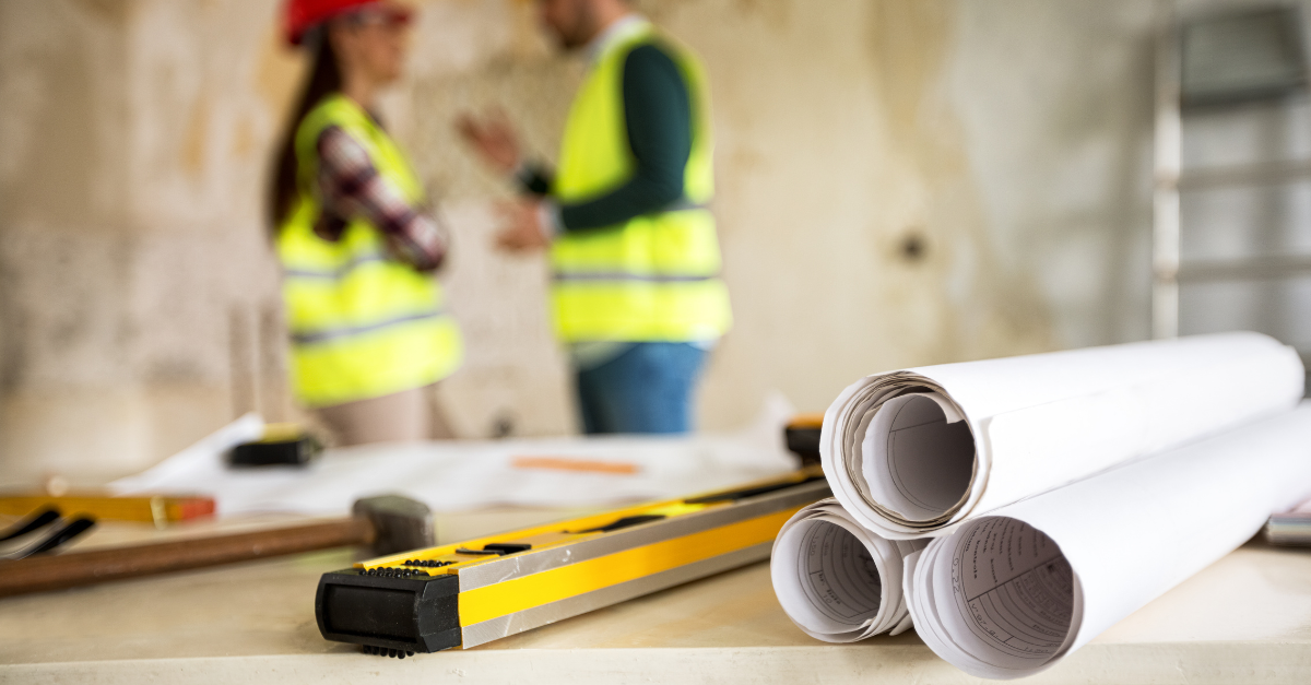 Two workers in hi-vis with rolls of plans and a spirit leveler.