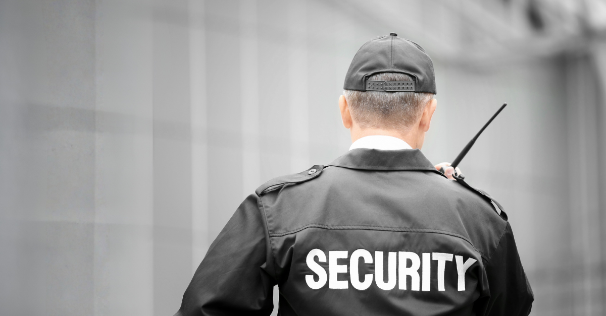 A security guard talking on his walkie talkie and wearing a cap.