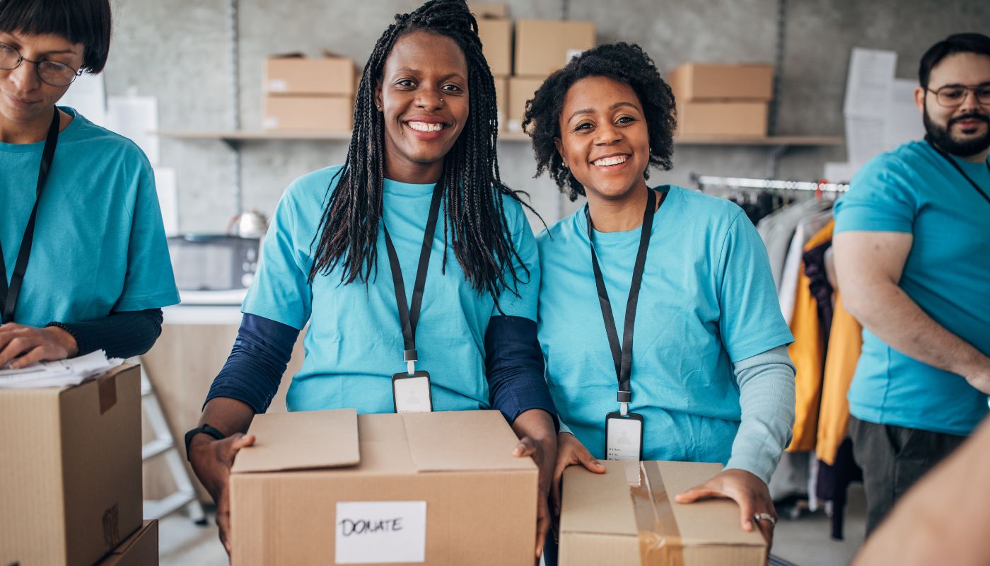 There are a group of voluntary workers holding boxes that say donate on and are wearing blue polo shirts with lanyards on smiling.