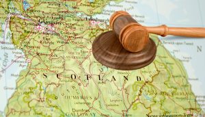 A map of Scotland with a gavel and a wooden block led on top of the map.