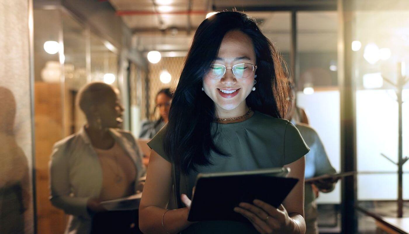 A business women looking at her tablet with a smile on her face, walking through the corridor of an office.