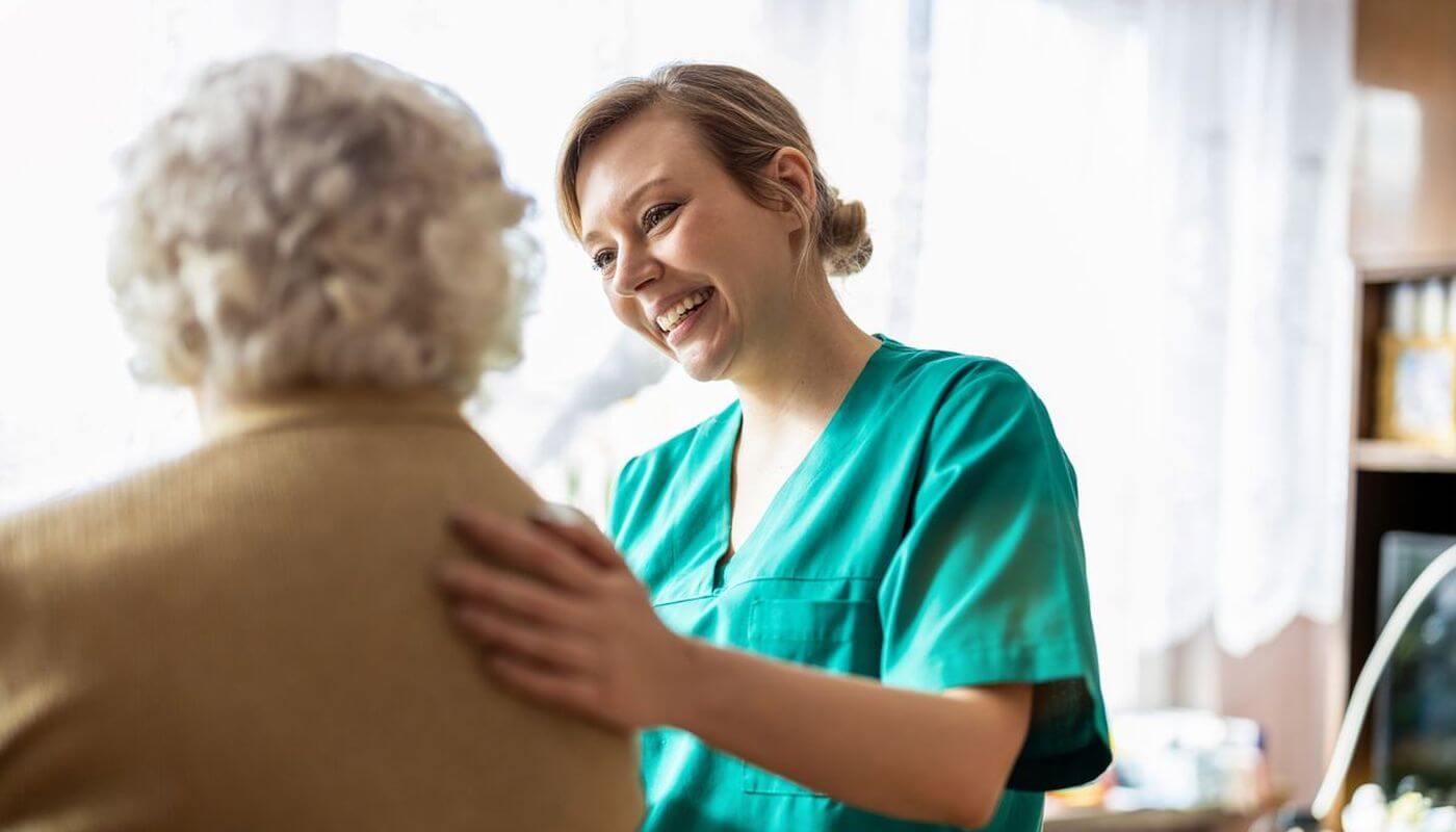 Care worker in green scrubs with her hand on the back of an elderly patient.