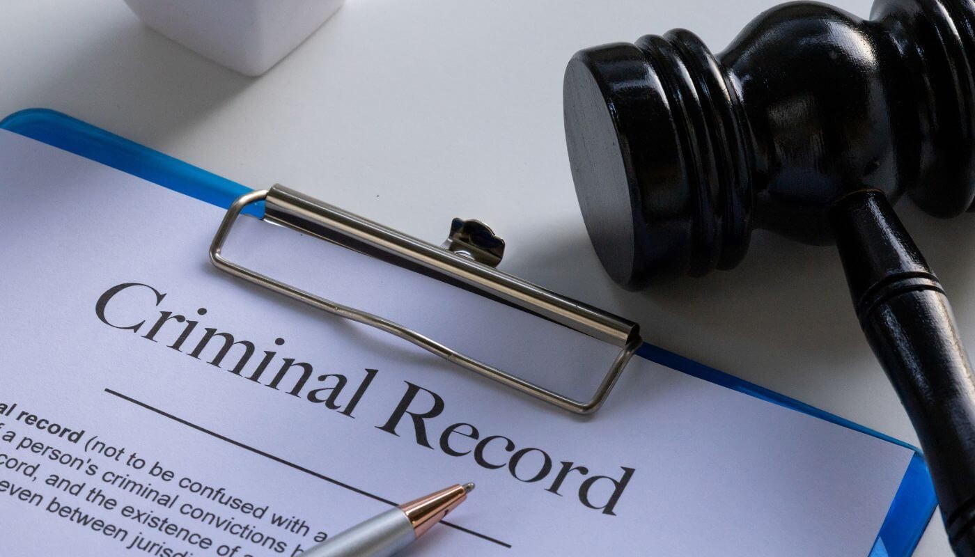 A piece of paper on a blue clipboard that says criminal record with a wooden gavel next to it.