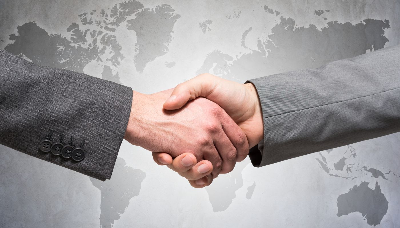 There are two men shaking hands in front of a world map on the wall.
