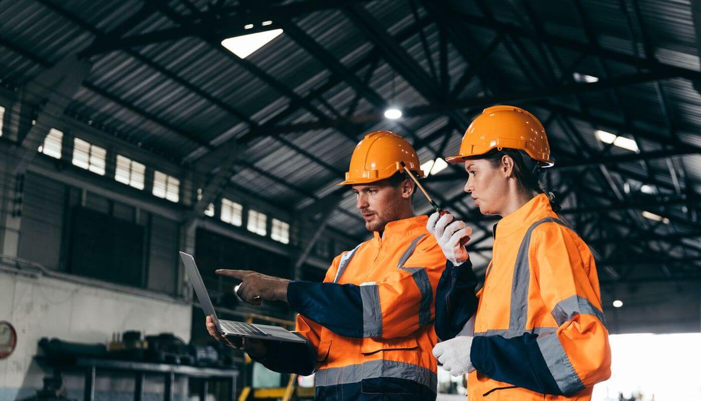 Two workers in a warehouse on laptop pointing at it.