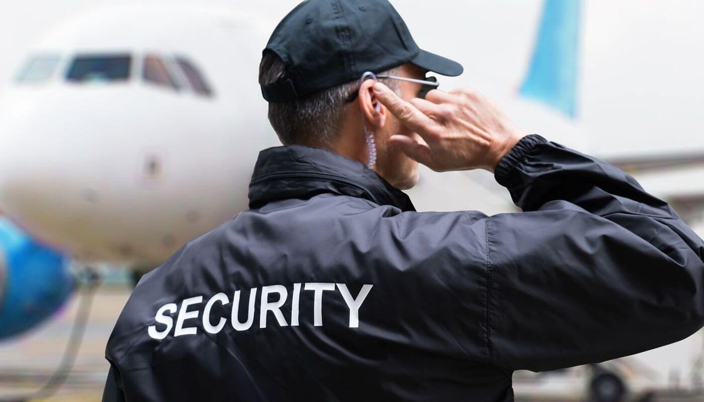A security guard is in front of a plane touching his earpiece.