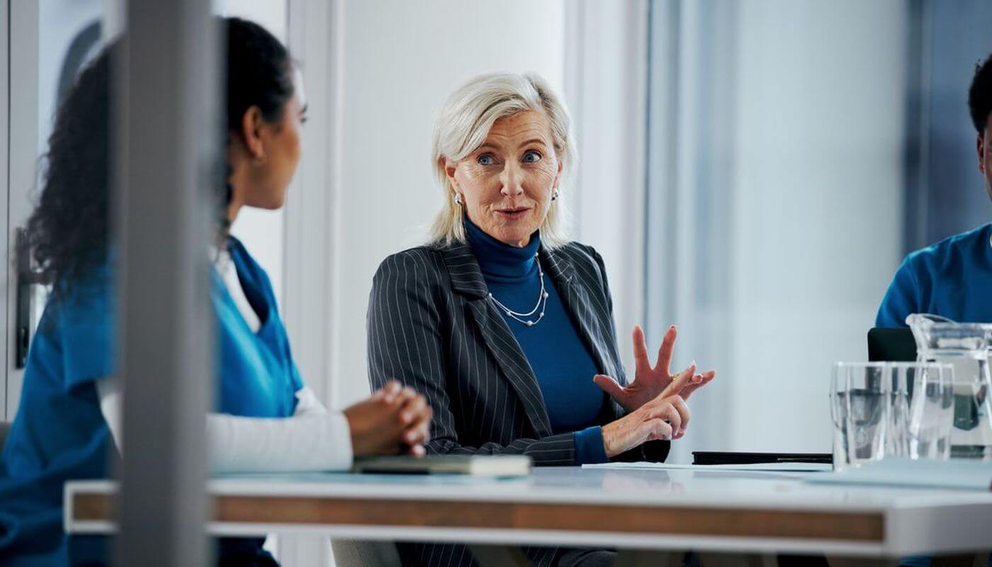 A senior business women having a meeting with a younger lady in blue scrubs in an office.