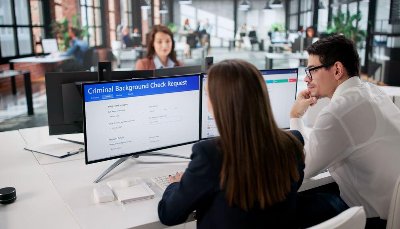Two staff members are reviewing a computer screen together that says criminal background checks.