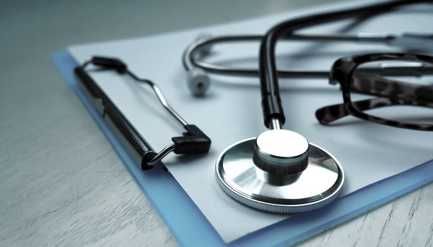 There is a clipboard on a desk with glasses and a stethoscope on top.