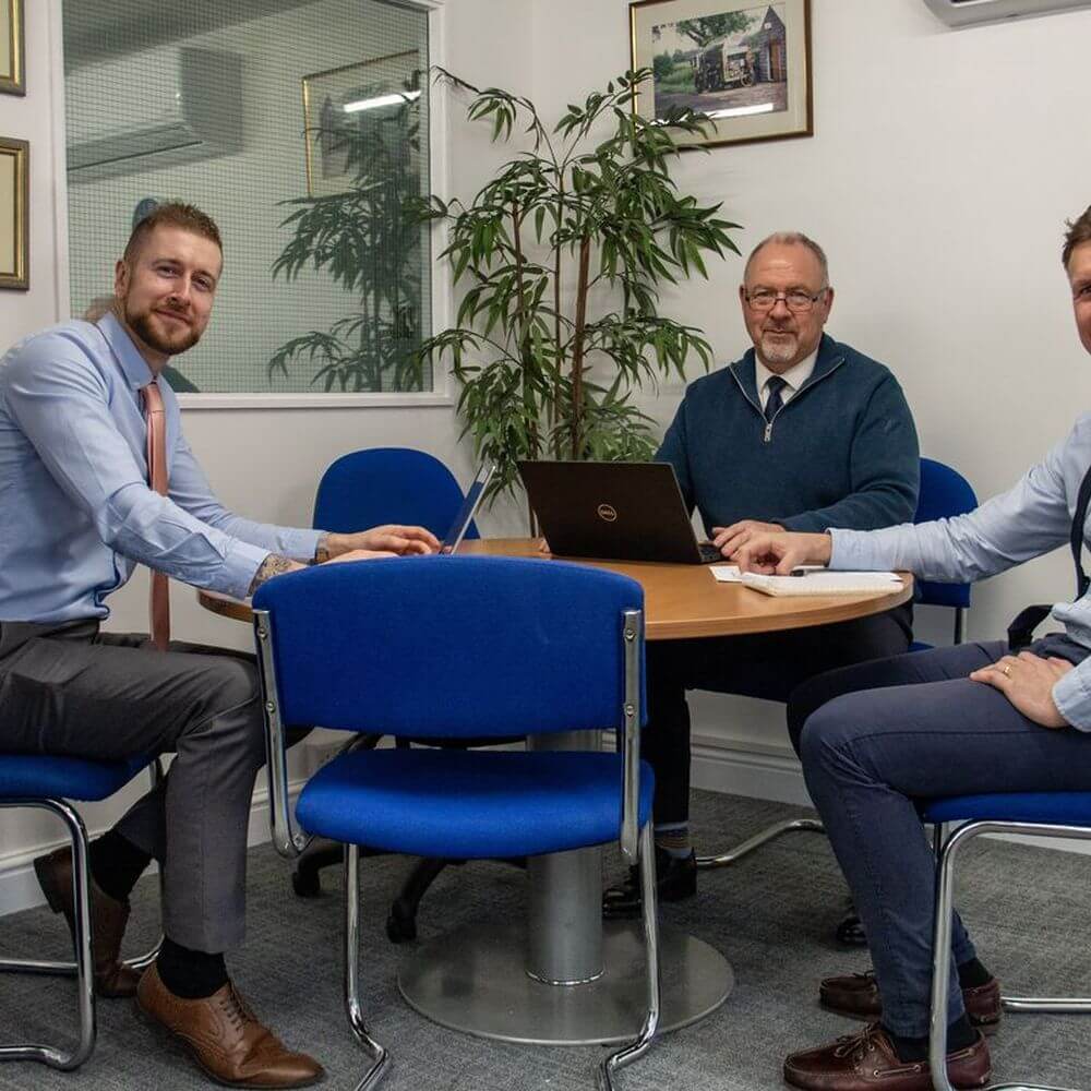 Three Security & Vetting Solutions staff members at a round table with laptop, pen and notepads.