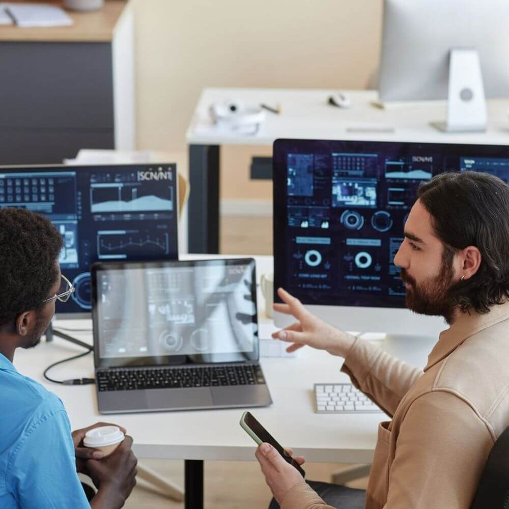 Two IT workers discussing the data on their laptop screens.